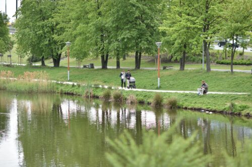 Staw, wzdłuż stawu poprowadzona jest ścieżka, widać spacerowiczów.