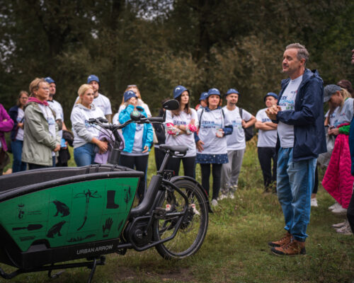 pan przemawia w parku przed grupą osób, na pierwszym planie stoi rower cargo