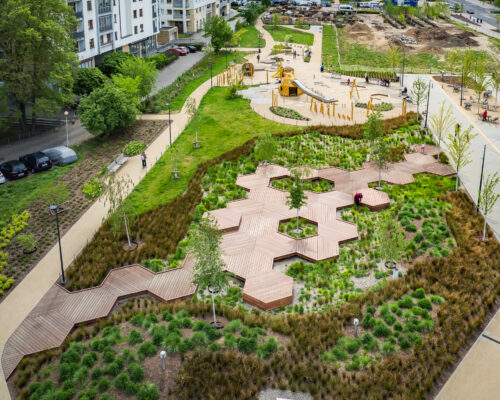 Ogród deszczowy, deptak drewniany w kształcie plastrów miodu, plac zabaw w tle - Park nad POW