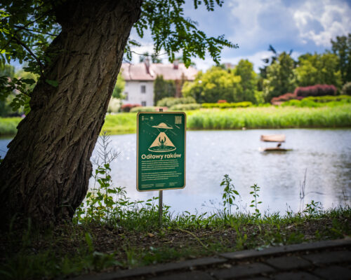 Zielona tabliczka z napisem "Odłów raków" - staw w tle