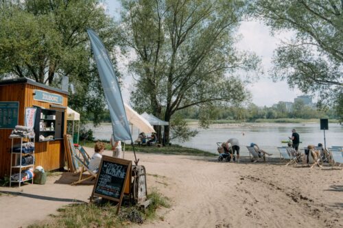 Punkt plażowy, baner Dzielnicy Wisła, ludzie nad rzeką, drzewa