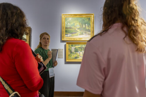Kobieta pokazuje coś osobom na obrazach w muzeum